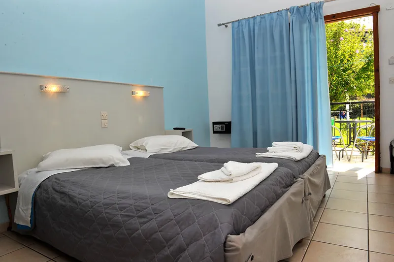 A twin room with a blue curtain and the balcony door open