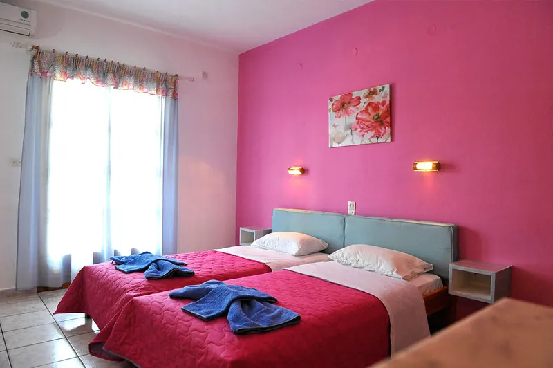 A twin room with a pink wall and a flower painting
