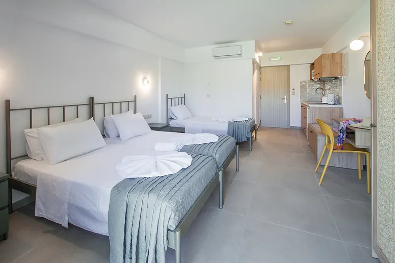 A room with three beds and a kitchenette by the door